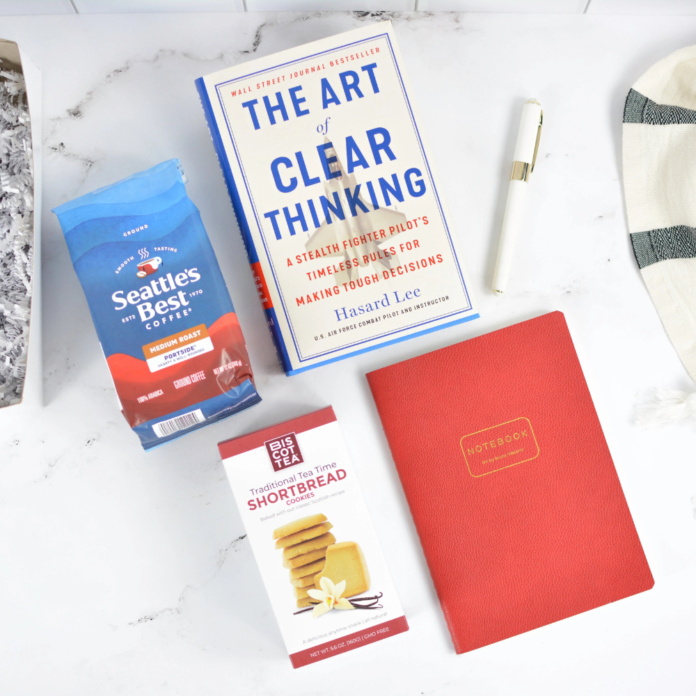 Book titled 'The Art of Clear Thinking' with a red notebook and coffee package on a marble surface.