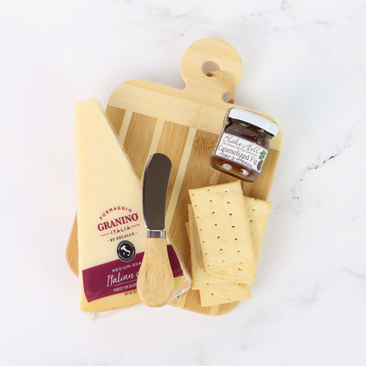 Wooden cutting board with cheese, a knife, and a jar of jam on a white surface
