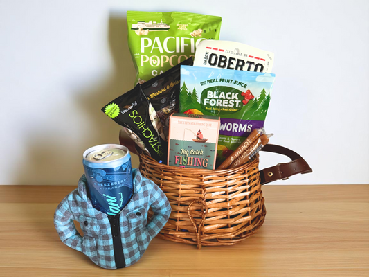 fishing gift basket shows drink koozie, gummy worms, fishing trivia, and snacks all assembled in a decorative fishing creel basket with strap