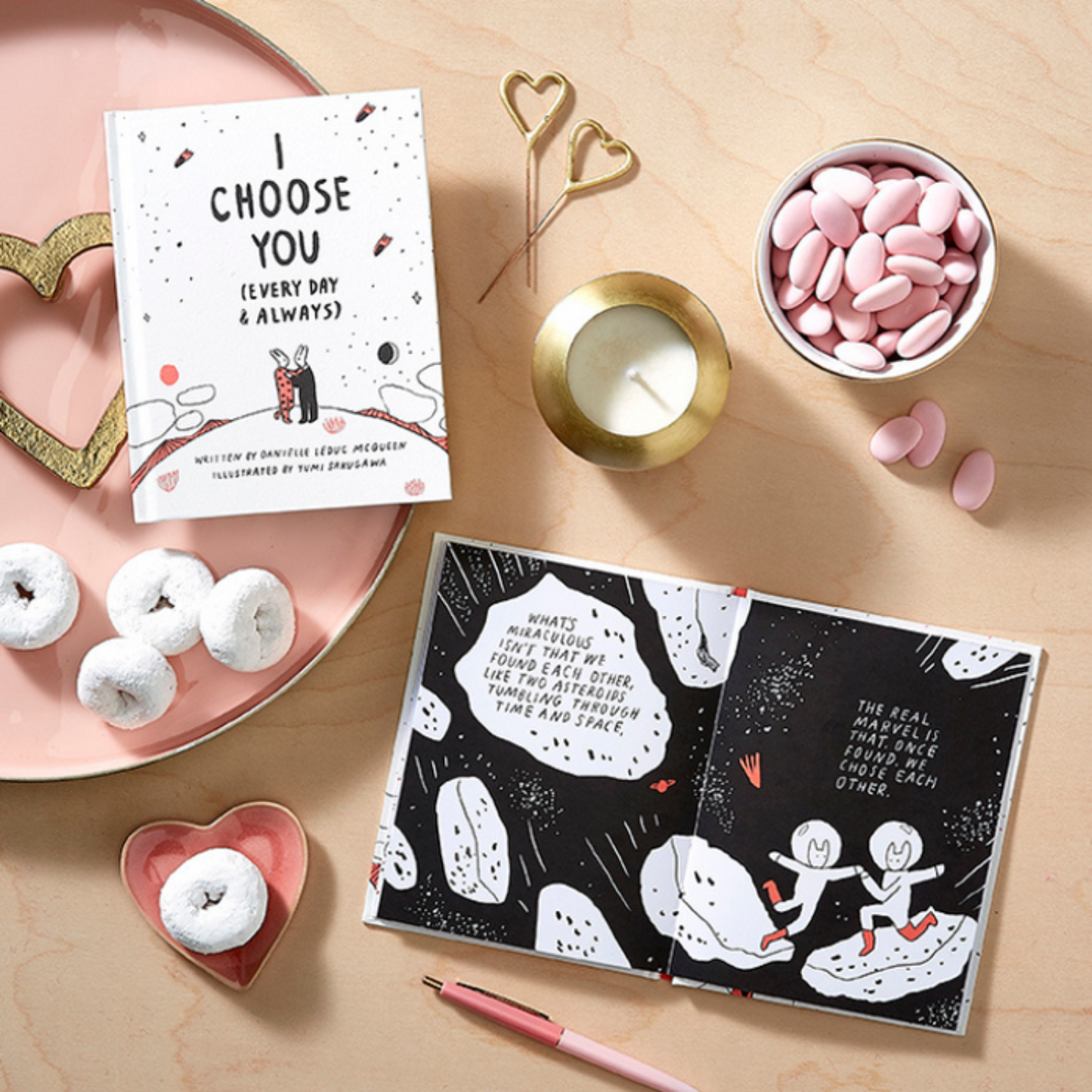 Valentine's Day-themed gift items including an i choose you book, card, donuts, and a candle on a wooden surface.