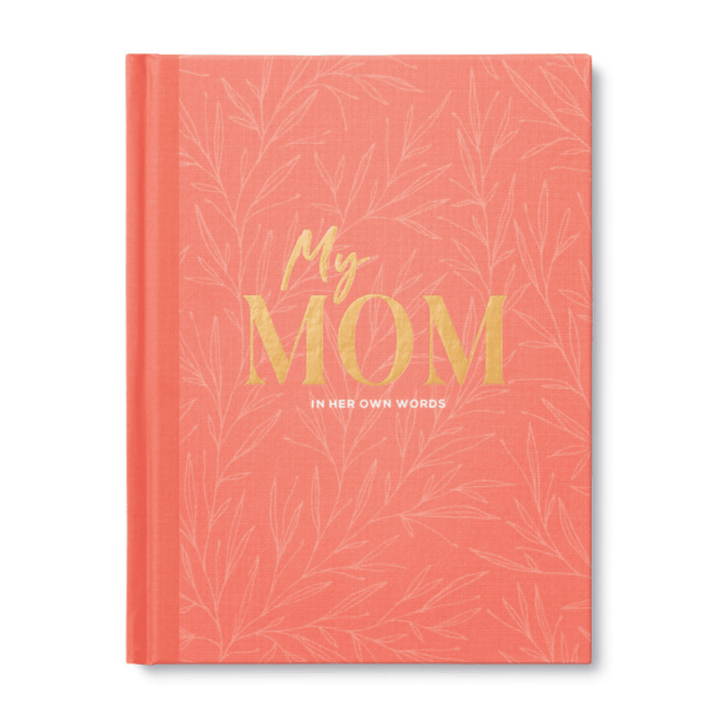Coral-colored hardcover journal titled "My Mom: In Her Own Words" with gold and white lettering, designed to help moms share memories and wisdom.