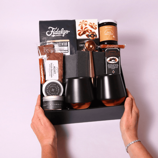 Luxury coffee gift box featuring Fidalgo organic whole bean coffee, Hot Cakes dark chocolate sauce, double-walled Fellow mugs, biscotti, caramels, and more in a sleek black box.