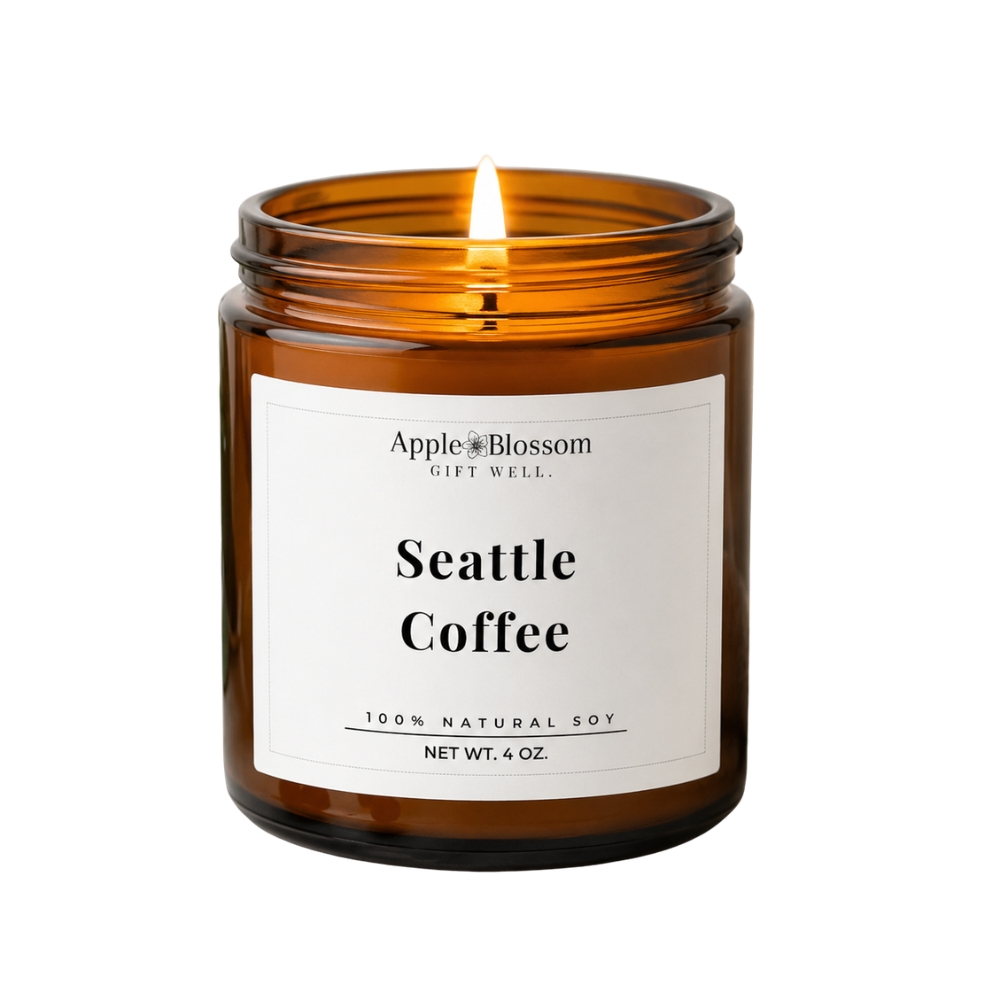 An amber glass jar candle with a white label reading 'AppleBlossom Gift Well. Seattle Coffee 100% Natural Soy' and a visible flame, isolated on a white background.