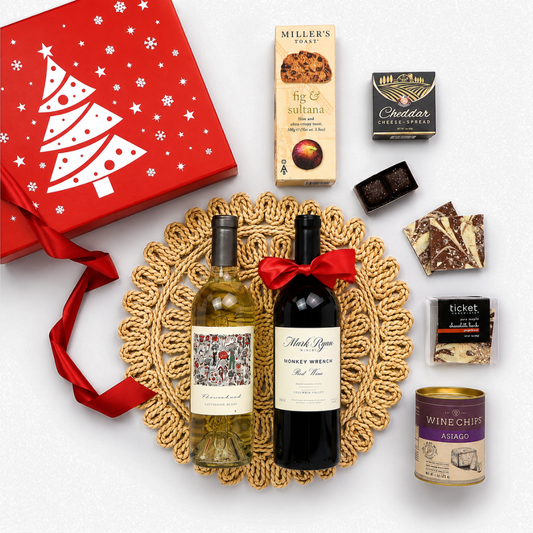 A curated gift hamper featuring a red Christmas-themed box with a white tree, a bottle of white wine, a bottle of red wine tied with a red ribbon, assorted chocolates, and a can of wine chiff, all arranged on a white background.