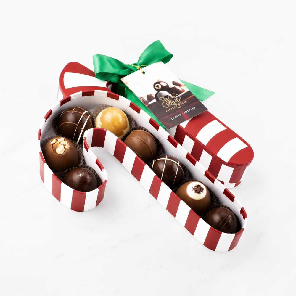 A candy cane shaped box of assorted chocolates arranged in a red and white striped candy cane shape, tied with a green ribbon and a chocolate tag, on a white marble background.
