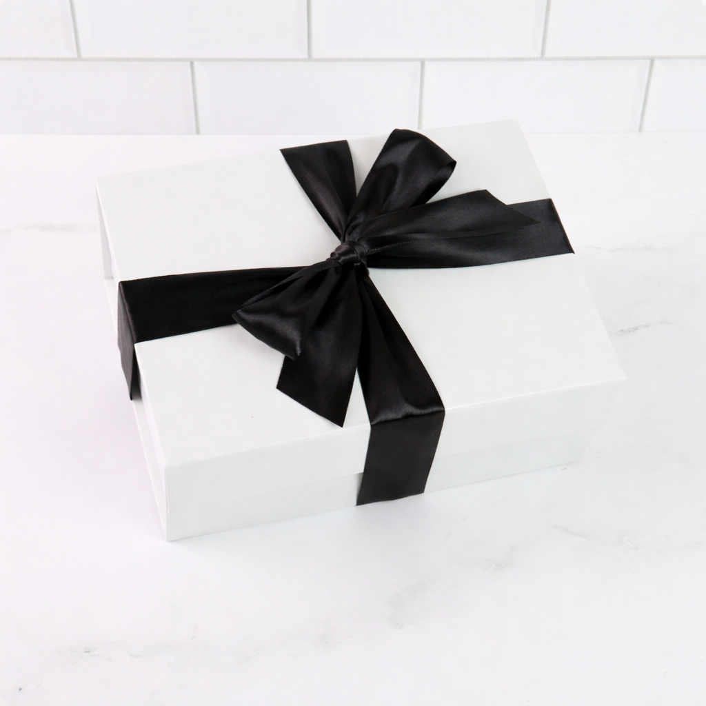 White gift box with a black ribbon on a white tiled background