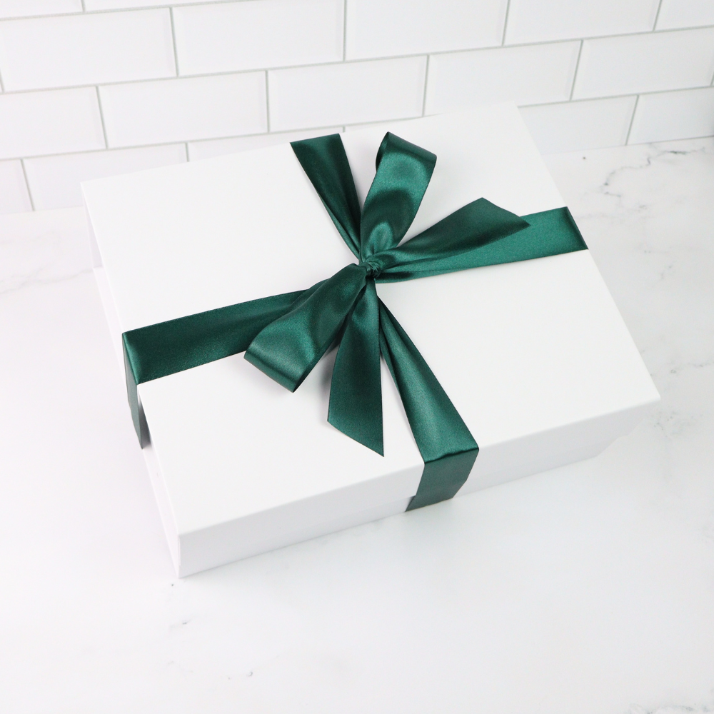 White gift box with a green ribbon on a white tiled background