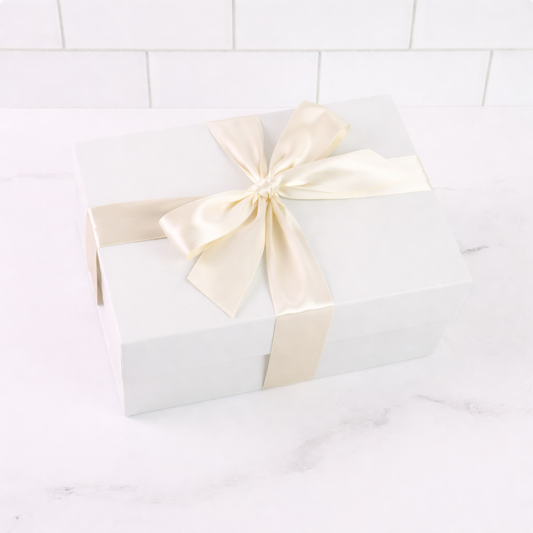 White gift box with a large cream ribbon on a white tiled background