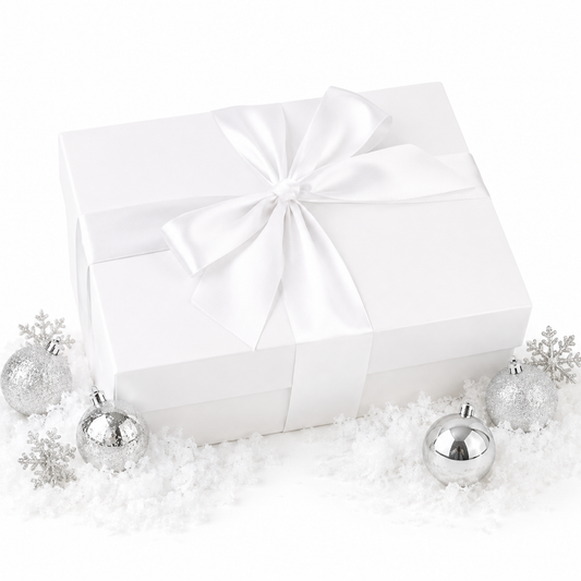 A white gift box wrapped with a large white satin ribbon and bow, styled on a white surface with scattered faux snow and silver holiday ornaments.