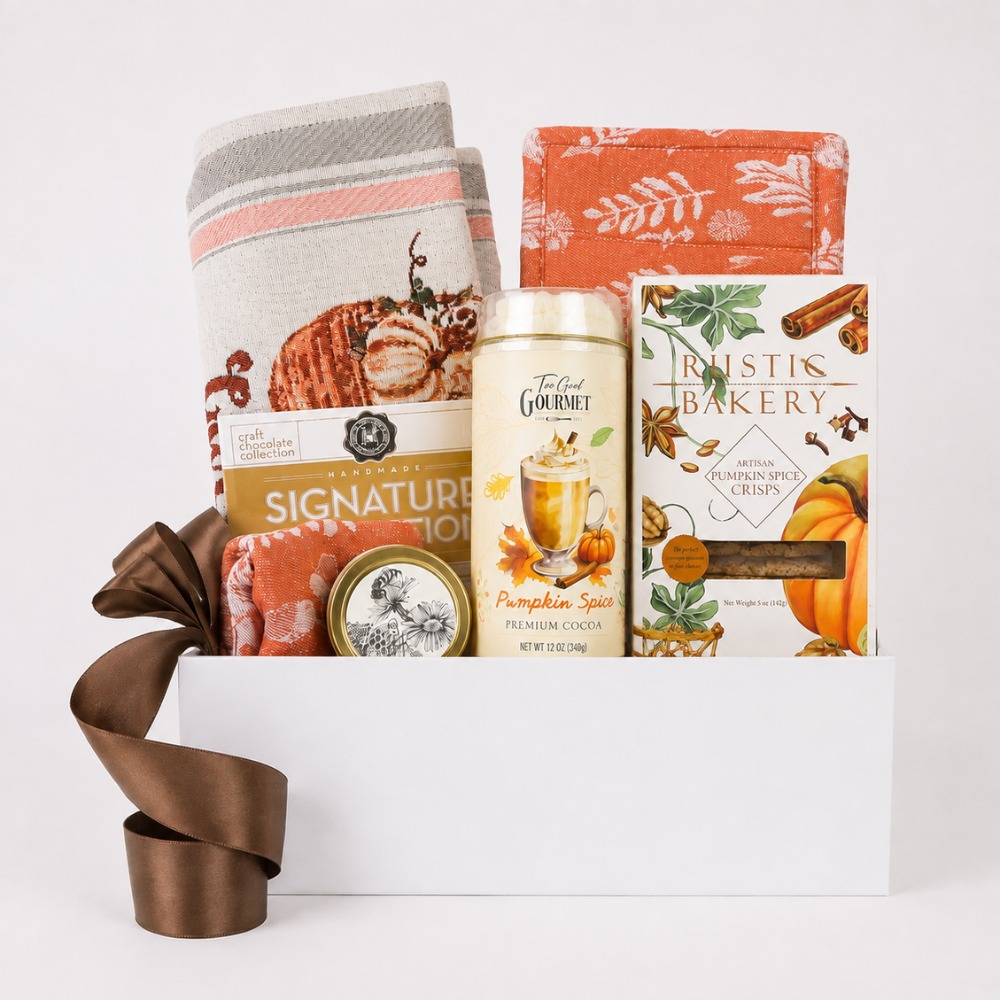 Fall gift basket featuring a kitchen towel with a pumpkin design, a can of Toffee Gourmet Pumpkin Spice Cacao, a box of Rustis Bakery Spiced Chews, and a small spice tin, styled with a brown ribbon bow on a white background.