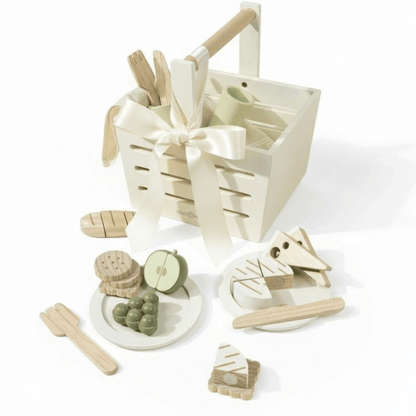 Wooden picnic basket with pretend fruit, crackers, bread, and utensils arranged in neutral tones.