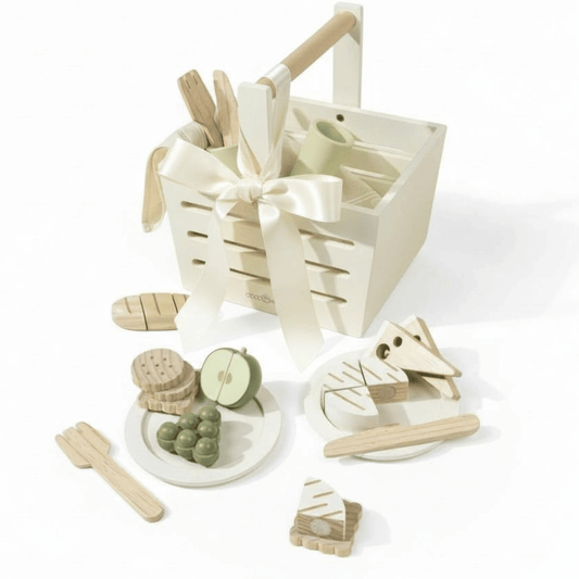 Wooden picnic basket with pretend fruit, crackers, bread, and utensils arranged in neutral tones.