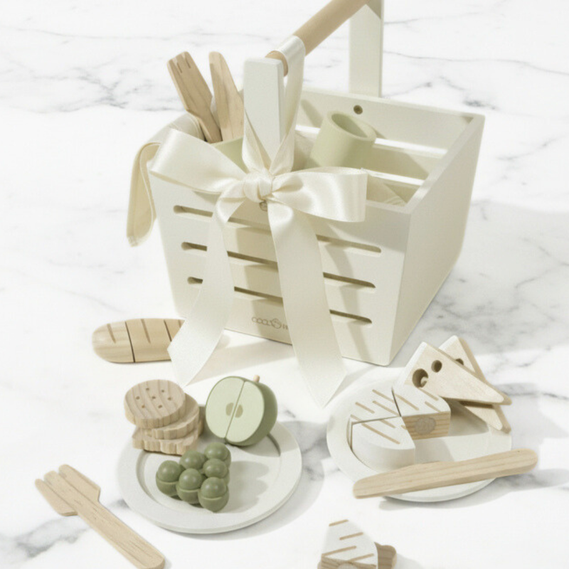 Wooden toys including a boat, fruits, and a basket with a bow on a white marble surface.