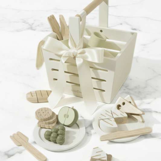 Wooden toys including a boat, fruits, and a basket with a bow on a white marble surface.