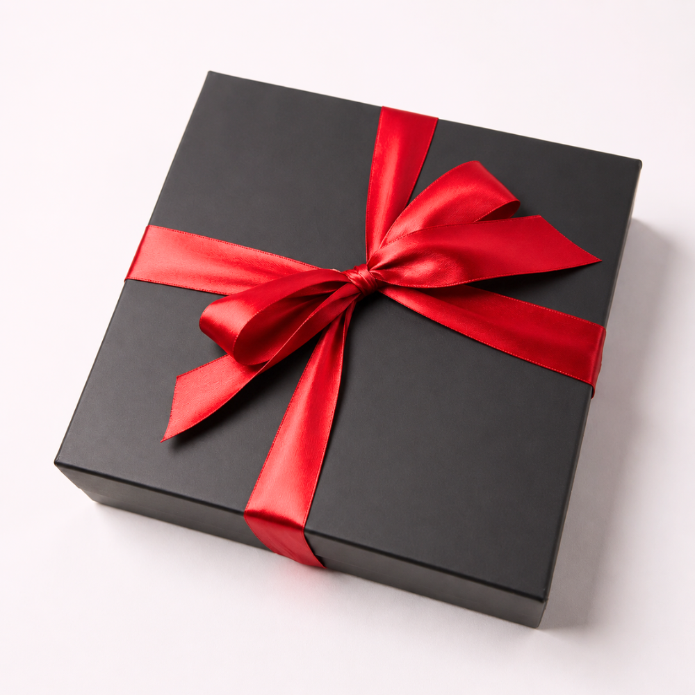 A square black gift box wrapped with a shiny red satin ribbon and bow, photographed on a clean white background.