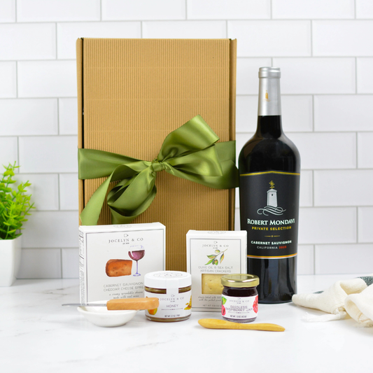Cabernet Sauvignon gourmet gift box with crackers, cheese spread, honey and preserves in gold ribbon packaging