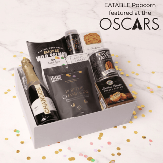 Gift box with Eatable Popcorn and other snacks on a white background with confetti.