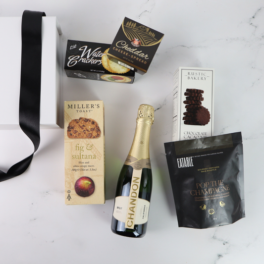 Bottle of Chandon champagne gift set with assorted snacks on a white surface
