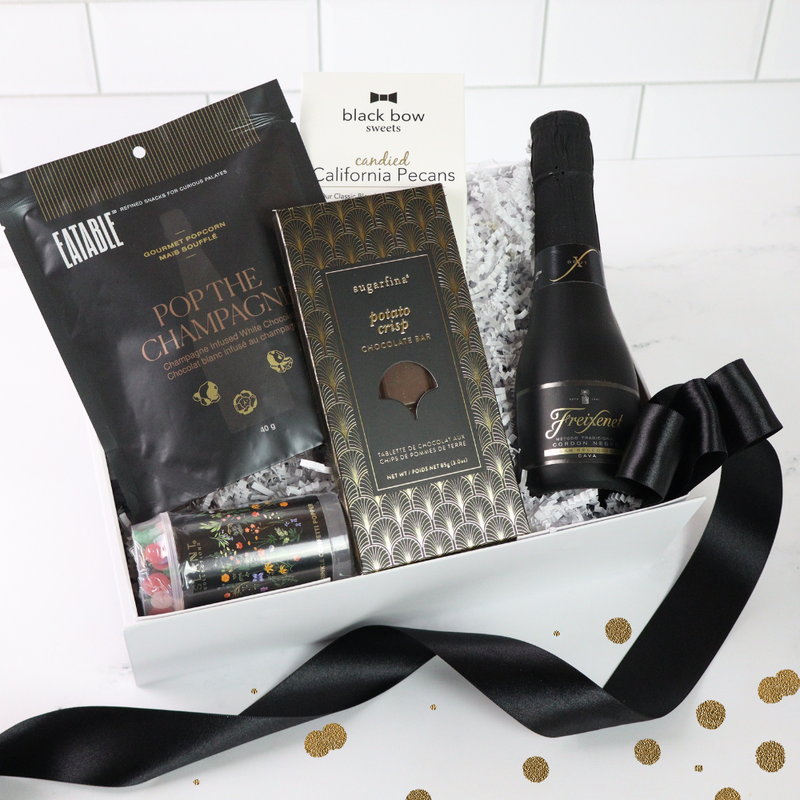 A luxurious celebration gift box featuring champagne-infused popcorn, a mini bottle of Freixenet, a Sugarfina chocolate bar, a confetti popper, and candied nuts, all elegantly arranged in a white box.