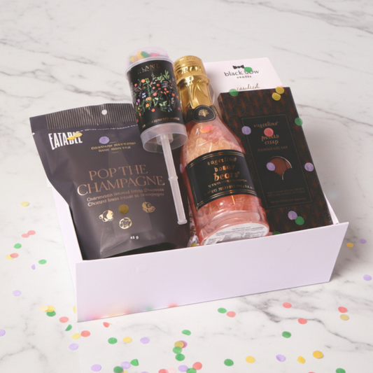 Luxury celebration gift box featuring champagne-infused popcorn, Sugarfina treats, a confetti popper, and a mini bottle of bubbly gummy bears.