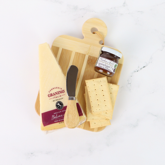 Wooden cutting board with cheese, a knife, and a jar of jam on a white surface