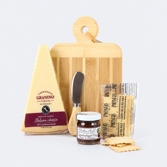 A gourmet cheese and crackers gift set arranged on a light gray background, featuring a wedge of Parmigiano d'Orino Italian cheese, a bamboo cutting board, a small cheese knife, a jar of prosciutto crudo, packaged prosciutto, and flatbread crackers.