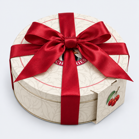 A round cream-colored gift box with a red satin ribbon bow and a cherry illustration on the side, photographed on a clean white background.