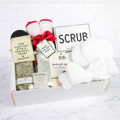 Day At The Spa Gift Basket Spa gift box filled with peppermint bath salts, pink scrunchie and cloth set, white headband, cleansing pads, konjac sponge, and SCRUB sponge—presented in a white box.
