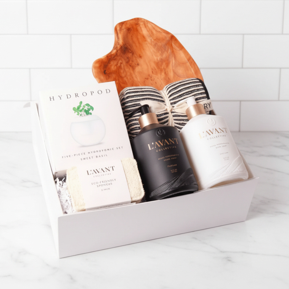 Luxury housewarming gift box featuring L'AVANT Collective high-performance hand and dish soap, a hydroponic basil growing kit, eco-friendly sponges, striped kitchen towels, and a stunning handcrafted wood serving board.