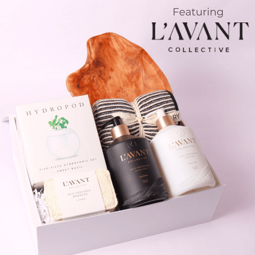 Luxury housewarming gift box featuring L'AVANT Collective high-performance hand and dish soap, a hydroponic basil growing kit, eco-friendly sponges, striped kitchen towels, and a stunning handcrafted wood serving board.