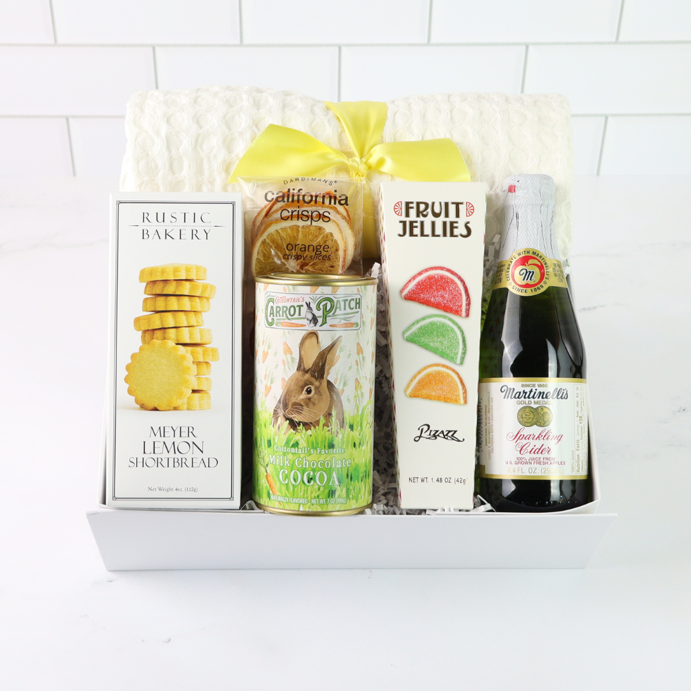 easter brunch Gift basket with various items including a bottle of sparkling cider, cookies, and a can of carrots on a white background.