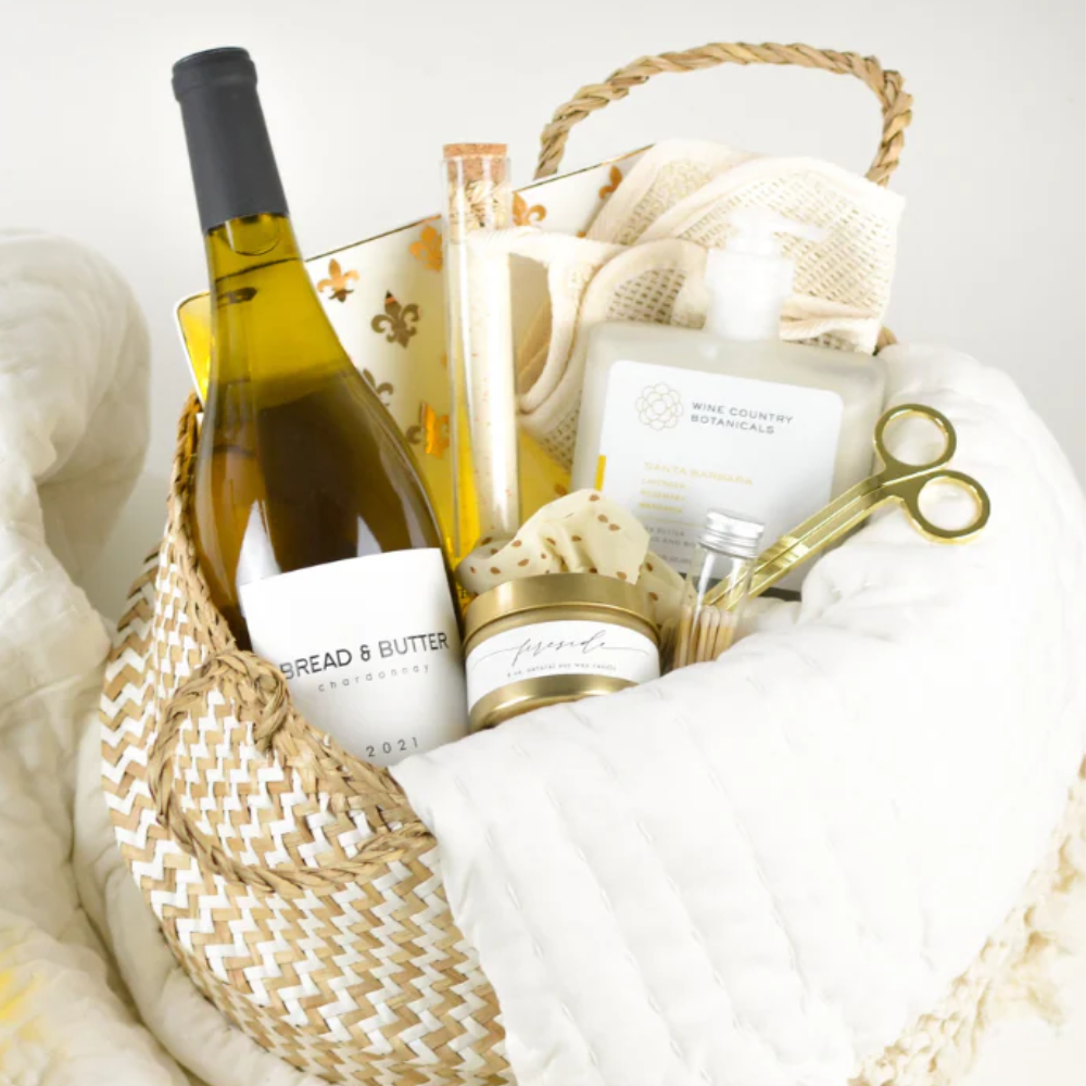Luxury wine and relaxation gift set featuring Bread & Butter Chardonnay, candle, cozy throw blanket, bath and body items, and gold accented accessories