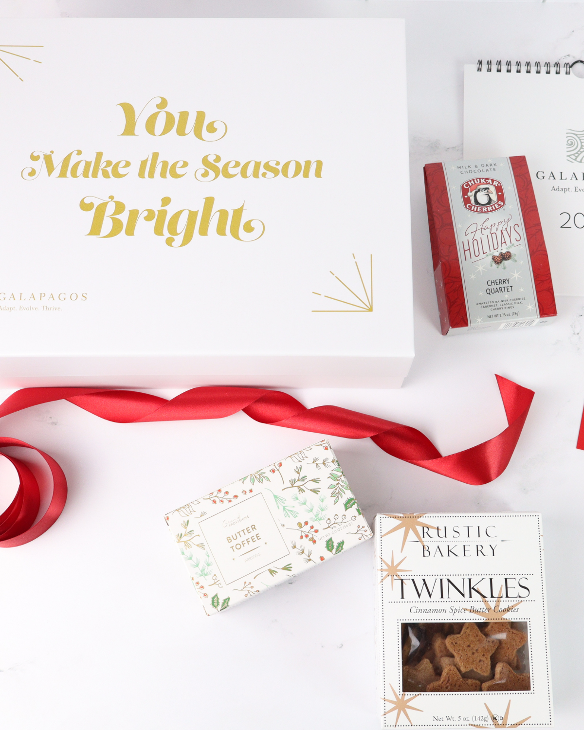 Luxury corporate holiday gift box flat lay featuring artisan treats, soy candle, and branded holiday card