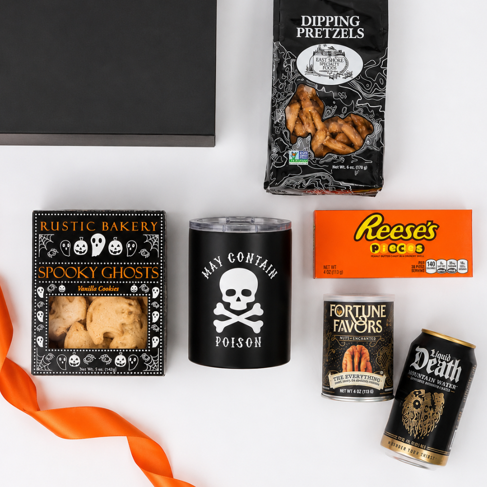 A Halloween-themed snack and gift box arrangement on a white background, featuring a black box, a bag of dipping pretzels, a black tumbler with a skull and crossbones, a box of Rustic Bakery Spooky Ghosts cookies, a Reese's PCC5 candy box, a can of Fortune Favors, a can of Jack Death Sour Apple Soda, and an orange ribbon.