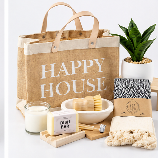 Happy House gift set with jute tote, faux plant, candle, dish bar, towel and wooden accessories on a clean light background