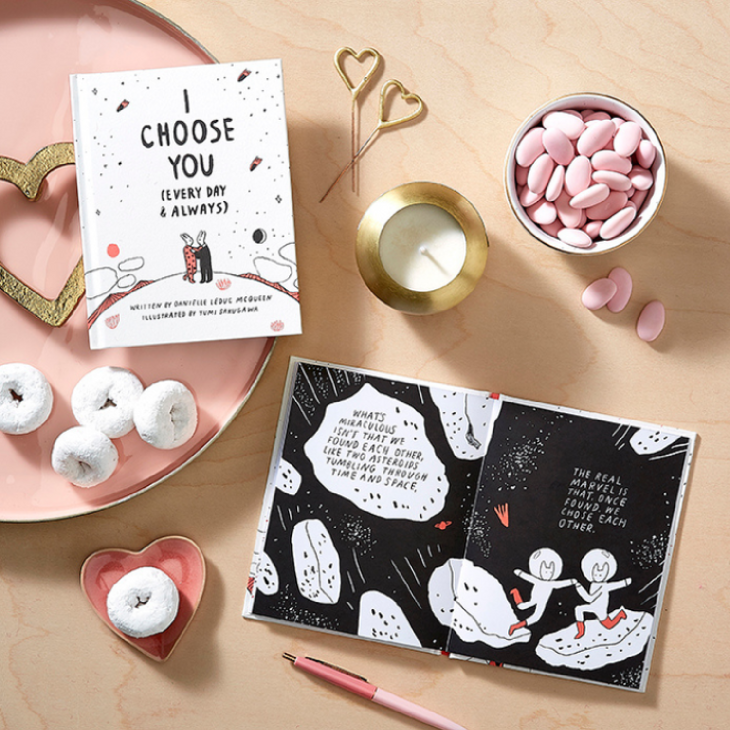 Valentine's Day-themed gift items including an i choose you book, card, donuts, and a candle on a wooden surface.