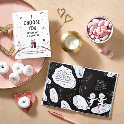 Valentine's Day-themed gift items including an i choose you book, card, donuts, and a candle on a wooden surface.