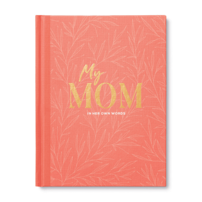 Coral-colored hardcover journal titled "My Mom: In Her Own Words" with gold and white lettering, designed to help moms share memories and wisdom.