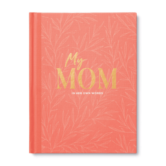Coral-colored hardcover journal titled "My Mom: In Her Own Words" with gold and white lettering, designed to help moms share memories and wisdom.