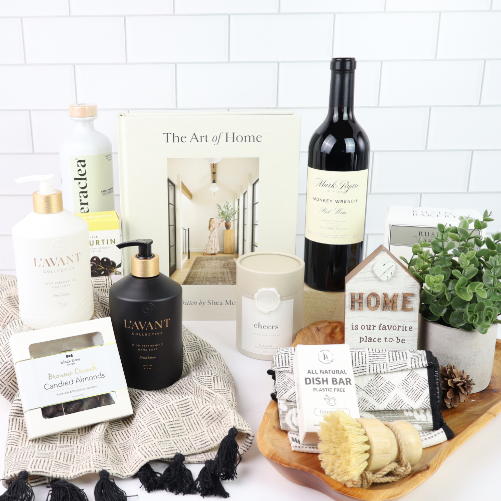 Collection of home products including a bottle of wine, candles, and soaps on a white surface with a 'The Art of Home' book.  Stunning luxury kitchen gift basket fro Seattle delivery.