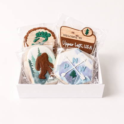 Pacific Northwest Cookie Gift Box with four hand-decorated cookies featuring Bigfoot, mountains, evergreen trees, and Upper Left USA design