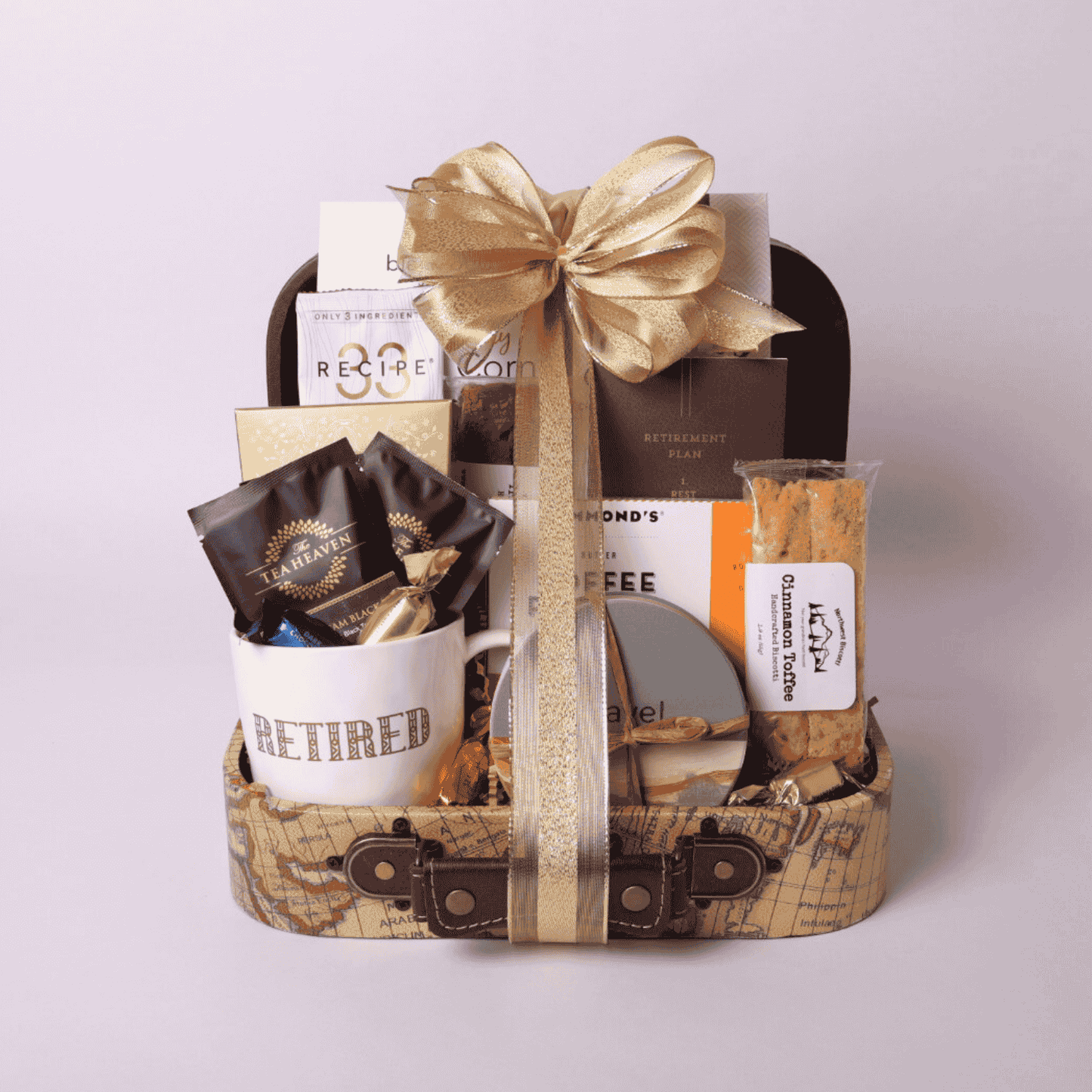 travel themed retirement gift basket in a mini suite case loaded with travel snacks, retirement mug, coasters and notebook with a gold bow.