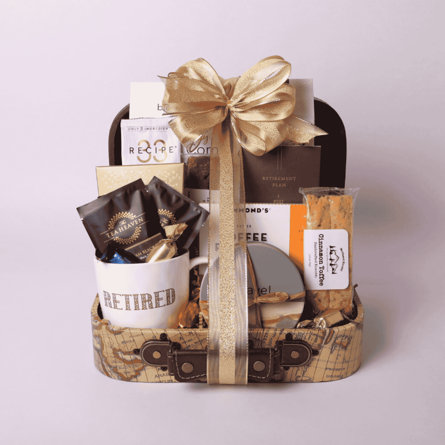 travel themed retirement gift basket in a mini suite case loaded with travel snacks, retirement mug, coasters and notebook with a gold bow.