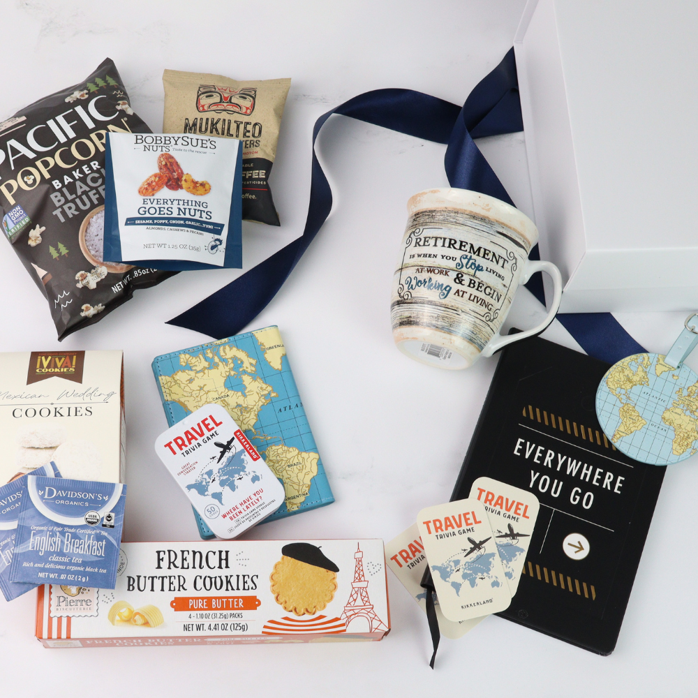retirement Gift box with travel-themed items including a retired mug, passport cover, luggage tag, book, cookies, and books on a white background