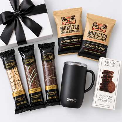 A gift set featuring a white gift box with a black ribbon, three Mukilteo coffee roaster bags, three Mukilteo biscuit bars, a black Swell travel mug, and a box of Aesthetic Bakery chocolate cak nibs, arranged on a white background.