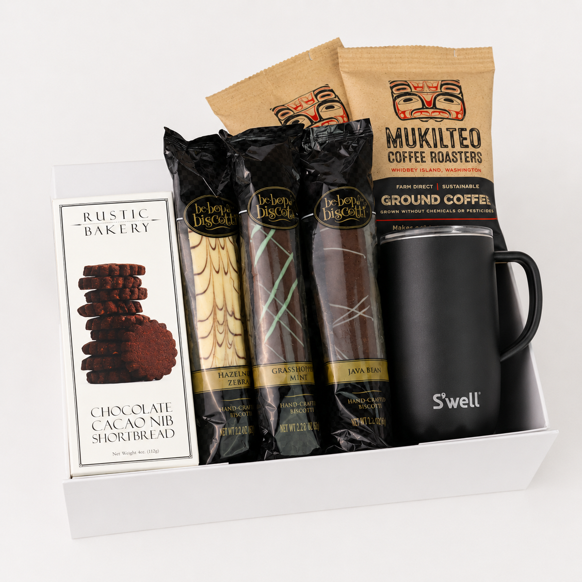 A curated gift box containing a box of Rustic Bakery chocolate cacao nib shortbread, three packages of Delia's Chocolate treats, two bags of Mukilteo coffee roasters, and a black S'well insulated tumbler.
