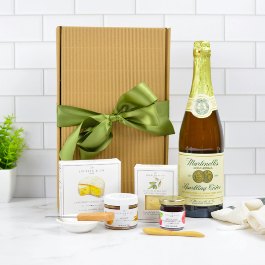 Sparkling cider gourmet gift box with artisan crackers, cheese spread, honey and jam in ribboned kraft packaging