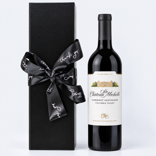 A bottle of Chantelle ste michelle Cabernet Sauvignon wine stands next to its tall black gift box tied with a black satin ribbon printed with 'thank you' in white script, on a light gray background.