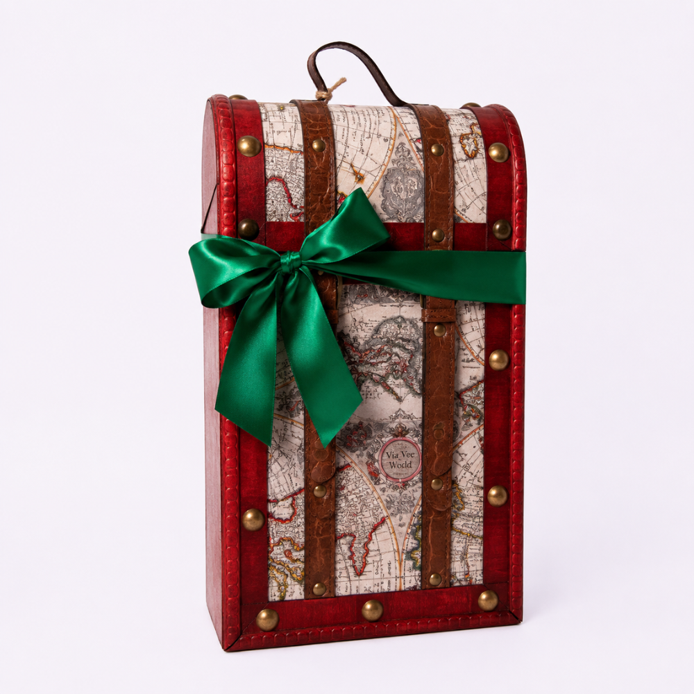 A vintage-style trunk-shaped gift box with a red leather-look exterior, brown straps, brass-tone studs, and an antique map print panel. A bright green satin bow is tied around the front, and a small handle is visible at the top, photographed on a clean white background.