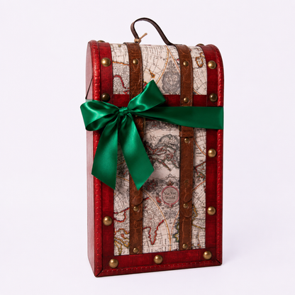 A vintage-style trunk-shaped gift box with a red leather-look exterior, brown straps, brass-tone studs, and an antique map print panel. A bright green satin bow is tied around the front, and a small handle is visible at the top, photographed on a clean white background.